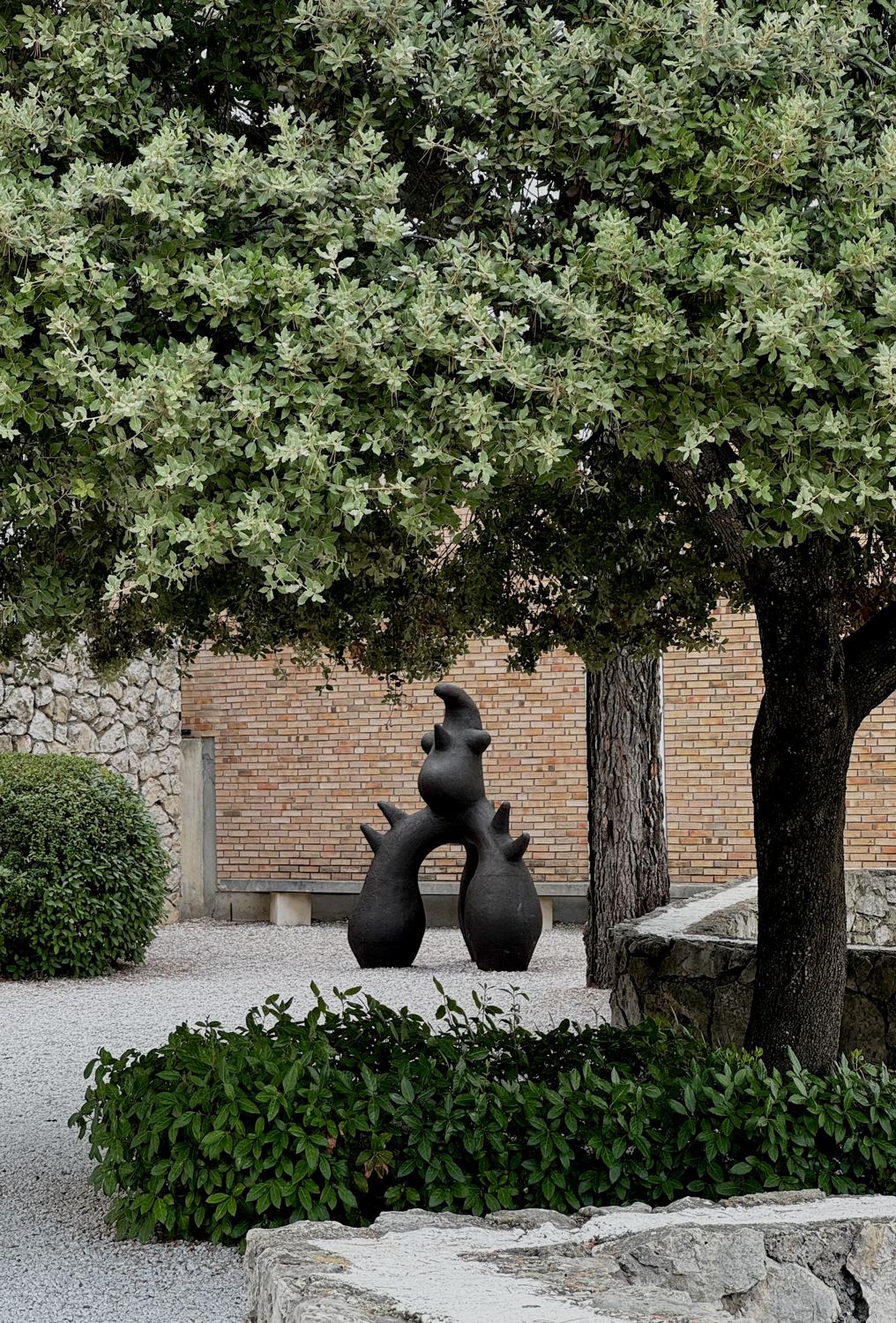 Black sculpture under a tree in the garden of Fondation Maeght
