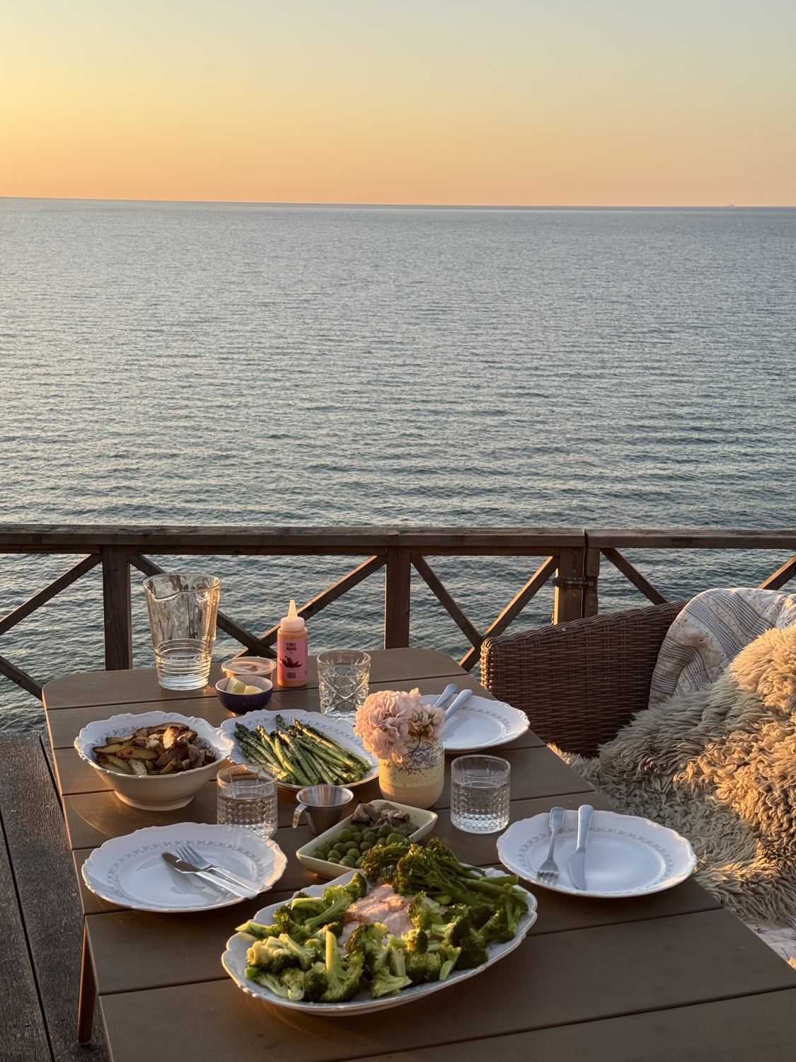 Dinner table on a wooden deck by the sea at sunset with asparagus, broccoli and potatoes